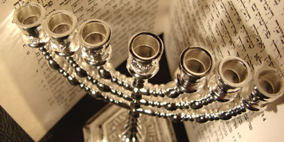 Das Bild zeigt ein Buch mit hebräischen Schriftzeichen, davor steht ein silberner Kerzenständer ohne Kerzen