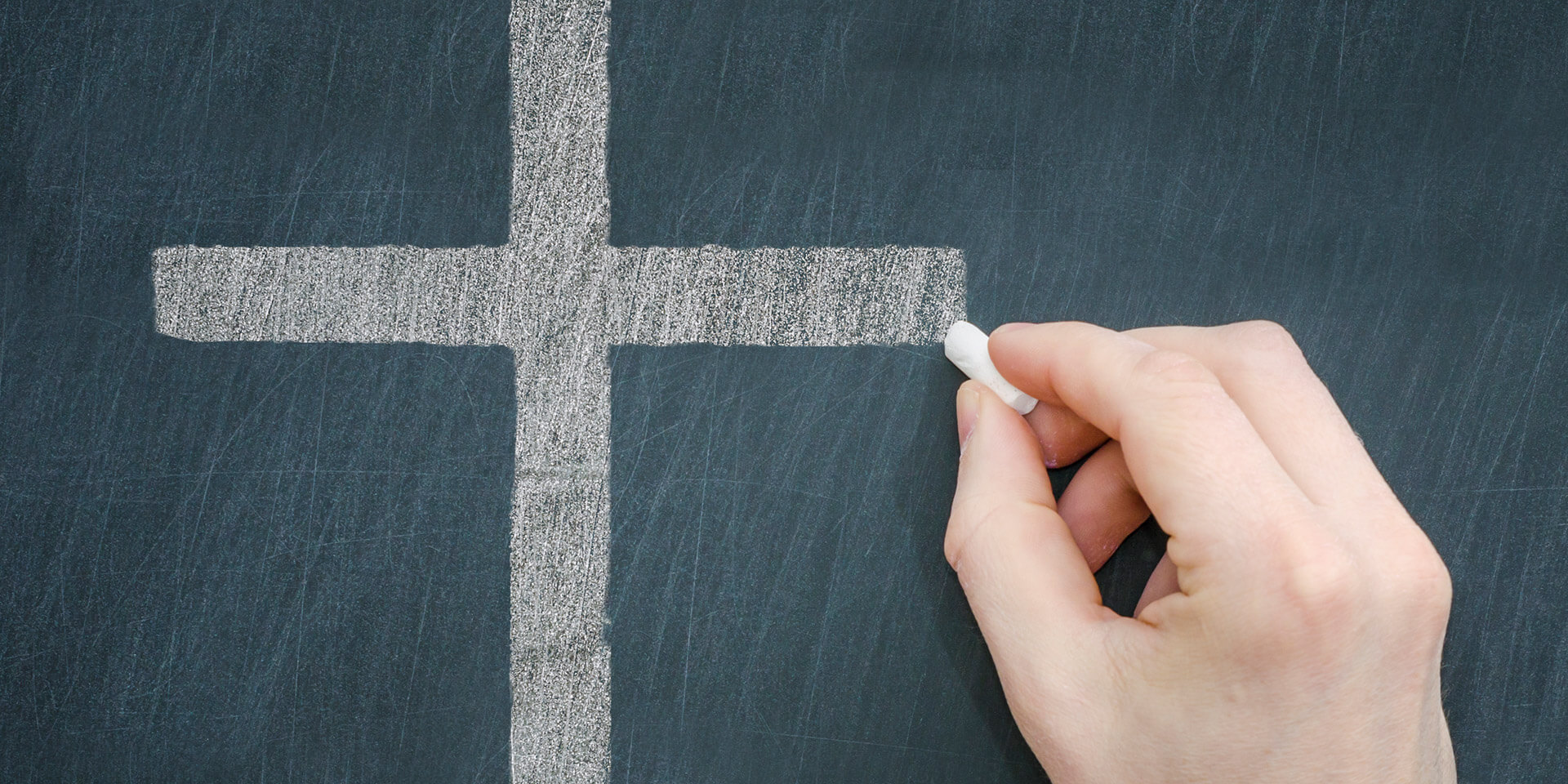 Das Bild zeigt eine Hand, die mit Kreide ein Kreuz an eine Tafel malt Eine Hand malt mit Kreide ein Kreuz an eine Tafel