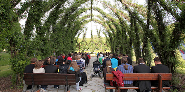 Menschen sitzen unter Weiden, die zu einem Kirchendach geformt sind, © Wolfgang Noack