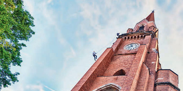 Das Bild zeigt einen Freeclimber, der wie ein Bergsteiger die Fassade einer Kirche emporklettert. Mensch klettert an Kirche empor