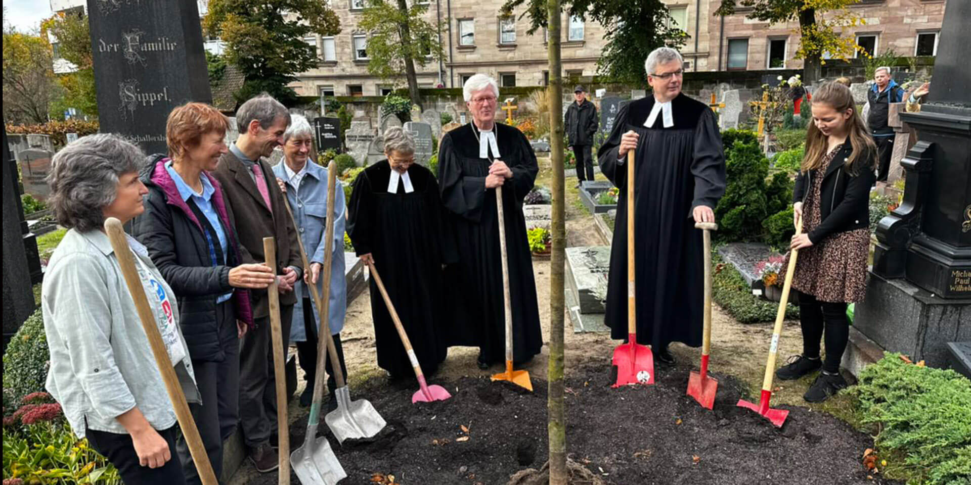 Mitglieder der Gemeinde St. Jobst und der Landesbischof pflanzen einen Baum auf dem Oasenfriedhof.