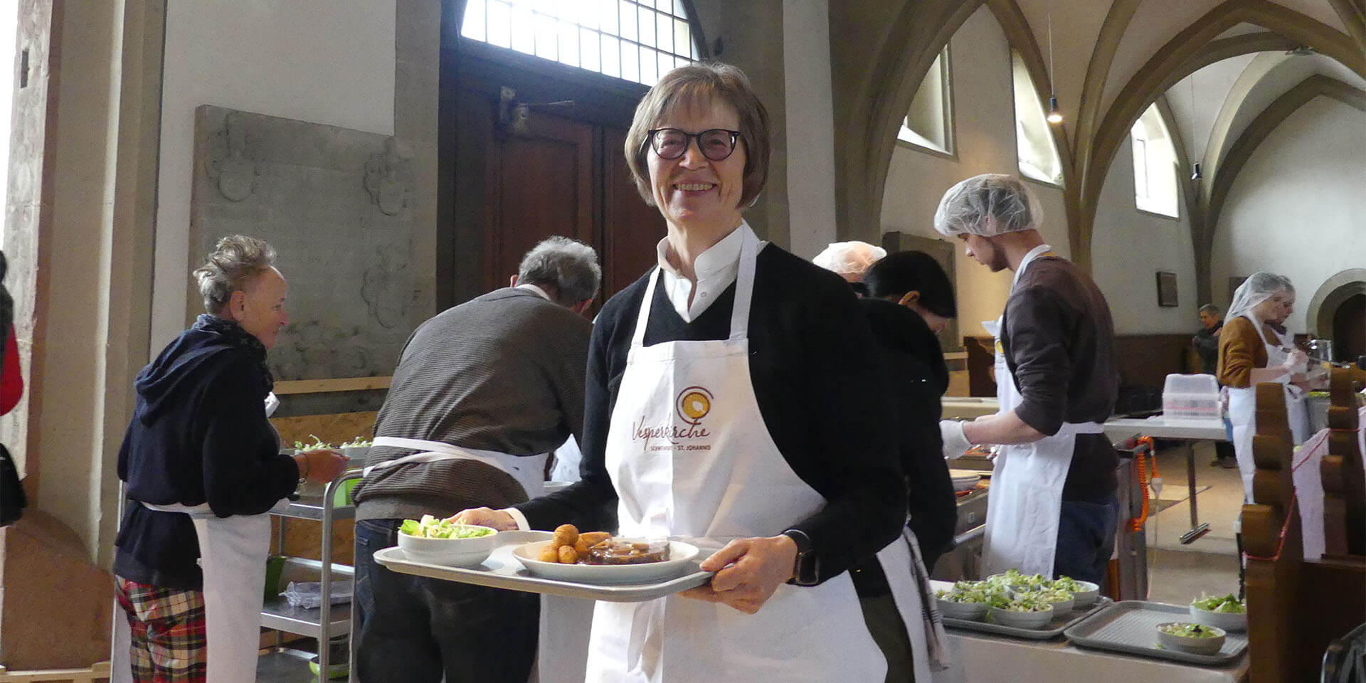 Regionalbischöfin Gisela Bornowski mit Schürze und Mahlzeit bei der Eröffnung der Vesperkirche in Schweinfurt