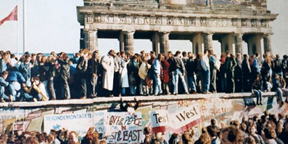 Menschen stehen nach historischem Mauerfall auf der Berliner Mauer. Im Hintergrund befindet sich das Brandenburger Tor